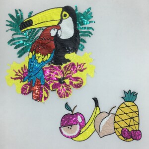 Pode incluir: Dois patches bordados coloridos. O primeiro patch apresenta um tucano com bico amarelo, um papagaio vermelho e azul, e uma flor rosa. O segundo patch apresenta uma banana amarela, uma maçã rosa, um pêssego e um abacaxi.