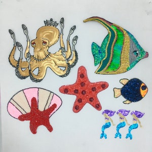 May include: A set of colourful, sequined iron-on patches featuring a variety of sea creatures, including an octopus, a starfish, a fish, a seashell, and mermaids.