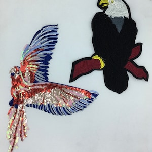 May include: Two embroidered iron-on patches featuring a red, pink, and blue bird with iridescent sequins and a black eagle with white head and yellow beak perched on a red branch.