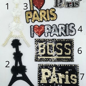 May include: A collection of decorative patches featuring the Eiffel Tower and the word "Paris". Patches include sequined designs with "I Love Paris" and "BOSS" text. Colors include gold, silver, red, and black.