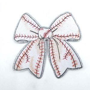 May include: A white baseball-themed bow with red stitching and a silver glitter outline. The bow is designed to resemble a baseball, with the red stitching mimicking the seams. This decorative bow is perfect for sports fans.