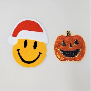 Peut inclure: Deux patchs en feutre, l'un un visage souriant jaune avec un chapeau de Père Noël rouge et l'autre une citrouille rouge, orange et noire en paillettes.