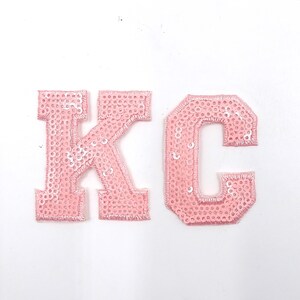 May include: Pink sequined iron-on patches in the shape of the letters K and C.