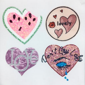 May include: Four sequined patches in the image. A watermelon slice, a circle with hearts and the word "lovely", a purple heart with "love", and a heart with "Don't Cry" and a crying eye.
