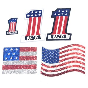May include: A collection of patriotic sequin patches featuring the American flag and the number "1". The patches include the flag in a rectangular and waving design, and the number "1" with red and white stripes and the word "USA".