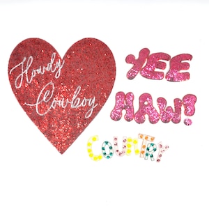 Puede incluir: Un corazón rojo brillante con el texto "Howdy Cowboy" en blanco, rodeado de letras brillantes de color rosa que deletrean "Yee Haw!" y letras brillantes multicolores que deletrean "Country".