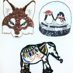 May include: Three embroidered iron-on patches: a brown fox head, a snow globe with two penguins, and a white elephant with colorful patterns.