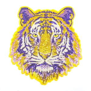 May include: A yellow and purple sequined tiger head applique. The tiger's face is detailed with purple stripes and a pink nose.