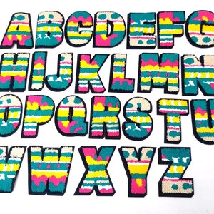 May include: A set of 26 colorful alphabet letters with a striped pattern. The letters are made of fabric and have a fuzzy texture. The letters are arranged in alphabetical order.