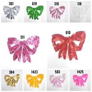 May include: Assortment of ten sequined bow appliques in various colors, including silver, green, pink, red, gold, orange, purple, and pink. Each bow has a unique number printed on it.