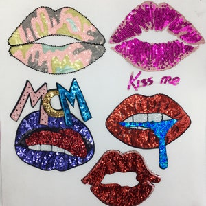 Op de afbeelding: Vijf strijkbare patches met lippen met pailletten. De patches zijn in verschillende kleuren, waaronder roze, rood, blauw en groen. Eén patch zegt "Kiss me" in cursief.