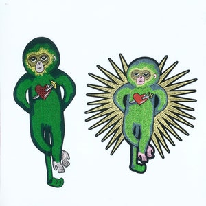May include: Two embroidered patches of green monkeys with red hearts pierced by swords. One monkey is surrounded by a golden halo.