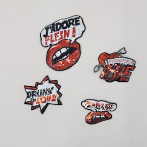 May include: Four iron-on patches with red and silver sequins. The patches feature the words "J'adore Plein", "Drunk in Love", "Love", and "Savile Row".