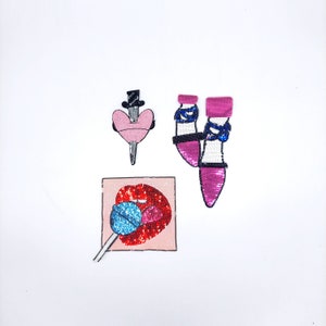 Puede incluir: Tres parches bordados que representan un corazón rosa con una daga, un par de tacones altos rosas y una boca roja con una piruleta azul.