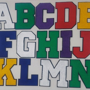 May include: A set of felt letter patches in various colors, including white, green, blue, purple, red, and yellow. The letters are in uppercase and range from A to N.