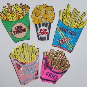 May include: A collection of sequined patches featuring fast food items. Includes a green container of fries with "WILD THINGS" text, a popcorn container with "POP CORN" text, and several "FRIES" containers in various colors.