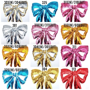 Könnte beinhalten: Zwölf verschiedene Pailletten-Schleifen-Patches in verschiedenen Farben, darunter Silber, Gold, Blau, Rosa und Rot. Jede Schleife hat eine andere Nummer darauf gedruckt, wie z. B. 301, 310, 311, 313, 325, 332 und 304.