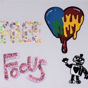May include: A colorful heart-shaped patch with dripping paint, a floral embroidered patch that says "FREE", a pink sparkly patch that says "Fools", and a black and white robot patch with a heart on its chest.