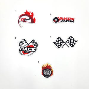 May include: Five iron-on patches with a racing theme. The patches feature a speedometer with flames, a tyre with the words "Racing Team", two chequered flags, a race car logo, and a tyre with flames.