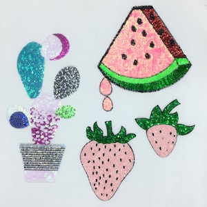 Può includere: Una collezione di toppe con paillettes raffiguranti un cactus in vaso, una fetta di anguria con succo che gocciola e due fragole. Le toppe sono nei toni del rosa, verde, nero e blu, su sfondo bianco.