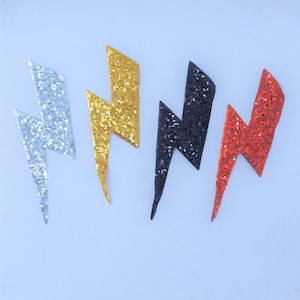 May include: Four sparkly lightning bolt iron-on patches in silver, gold, black, and red.