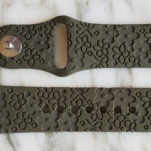 May include: A green silicone watch band with a floral pattern. The band has a textured surface and a metal buckle.