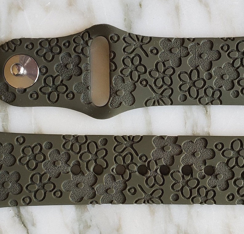 May include: A green silicone watch band with a floral pattern. The band has a textured surface and a metal buckle.