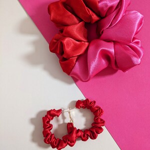 Puede incluir: Una scrunchie de sat&eacute;n rojo y rosa y pendientes de aro de sat&eacute;n rojo a juego. La scrunchie est&aacute; dividida en dos colores, rojo y rosa. Los pendientes tienen postes dorados.