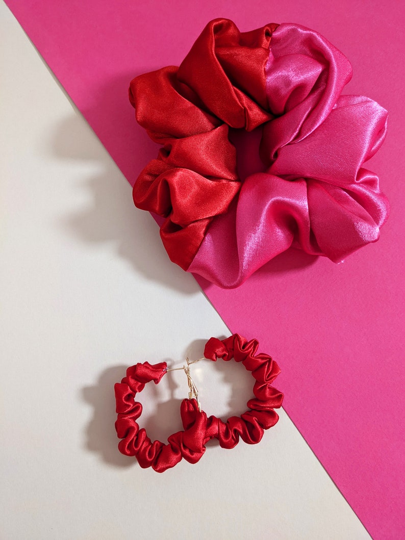 Puede incluir: Una scrunchie de sat&eacute;n rojo y rosa y pendientes de aro de sat&eacute;n rojo a juego. La scrunchie est&aacute; dividida en dos colores, rojo y rosa. Los pendientes tienen postes dorados.