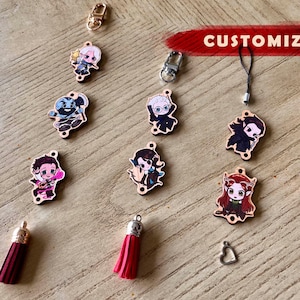 May include: A collection of customizable charms and accessories, including character pendants, tassels, and metal beads. The pendants feature colorful anime-style illustrations. The word "CUSTOMIZABLE" is displayed in red.