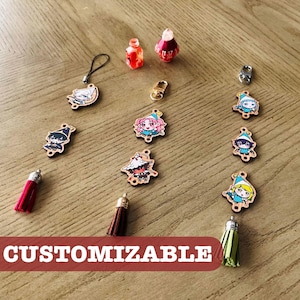 May include: A collection of wooden charms featuring colorful anime-style character illustrations, including various figures with hats, small red and pink potion-shaped charms, metal clasps, and fabric tassels in red, brown, and green colors.