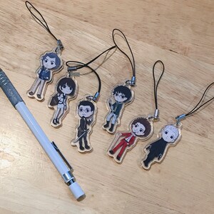 May include: Seven colorful character charms with black string lanyards. The charms are made of clear plastic with printed images of people. The characters are all different and have unique hairstyles and clothing.
