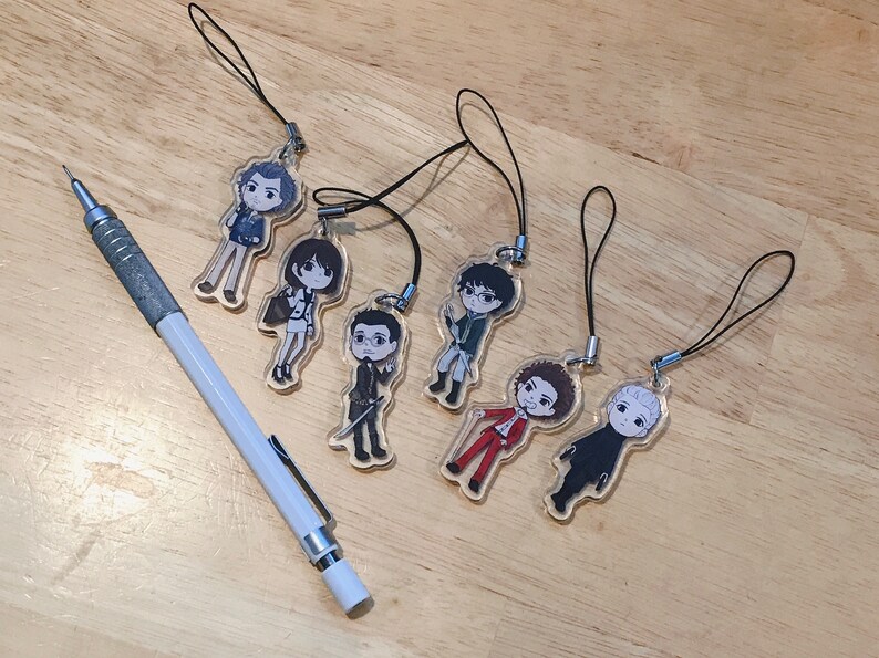 May include: Seven colorful character charms with black string lanyards. The charms are made of clear plastic with printed images of people. The characters are all different and have unique hairstyles and clothing.