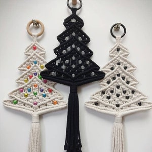 May include: Three macrame Christmas tree wall hangings with different coloured beads. The tree on the left has rainbow coloured beads, the middle tree has black beads, and the tree on the right has black beads.