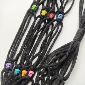 May include: A black macrame cord net with colorful skull beads. The net is knotted and has a fringe at the bottom. The skull beads are in various colors, including purple, blue, orange, pink, yellow, and green.
