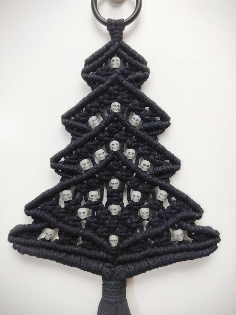 K&ouml;nnte beinhalten: Schwarzer Makramee-Weihnachtsbaum-Wandbehang mit wei&szlig;en Totenkopfperlen.