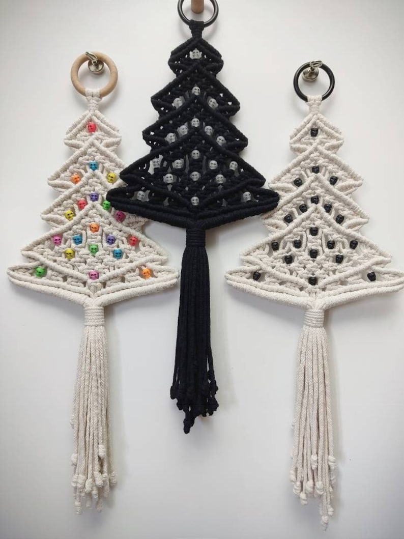 K&ouml;nnte beinhalten: Drei Makramee-Weihnachtsbaum-Wandbeh&auml;nge mit unterschiedlichfarbigen Perlen. Der Baum links hat regenbogenfarbene Perlen, der mittlere Baum hat schwarze Perlen und der Baum rechts hat schwarze Perlen.