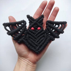 May include: Black macrame bat wall hanging with red bead eyes.