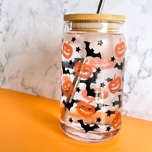 May include: A clear glass reusable water bottle with a bamboo lid and a stainless steel straw. The bottle is decorated with a Halloween theme featuring black bats and orange pumpkins.