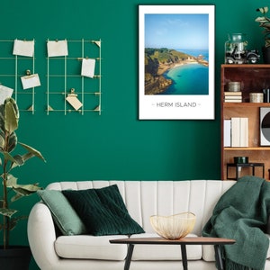 Puede incluir: Un sof&aacute; blanco con cojines y una manta verdes, un cuenco de alambre dorado sobre una mesa de caf&eacute; de madera, y una foto enmarcada de un paisaje costero con el texto "Herm Island" en una pared verde.