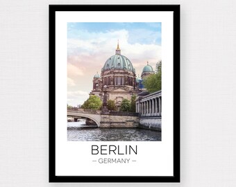May include: A framed print of a photograph of the Berliner Dom, a large church in Berlin, Germany. The church is a prominent landmark in the city and is known for its distinctive dome. The photo shows the church from a distance, with a bridge and river in the foreground. The print is titled "BERLIN - GERMANY -" in black text.