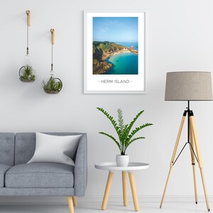 Puede incluir: Una fotograf&iacute;a enmarcada de un paisaje costero con una bah&iacute;a azul turquesa y una costa rocosa. El texto "Herm Island" est&aacute; impreso debajo de la imagen.