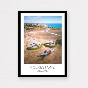 May include: An aerial view of three vintage aircraft on display at a park in Folkestone, England. The planes are painted in camouflage colours and are surrounded by green bushes. The park is located on a cliff overlooking the sea.
