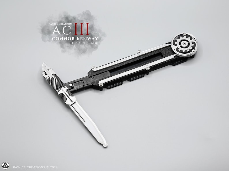 K&ouml;nnte beinhalten: Eine schwarze und silberne versteckte Klingen-Requisite aus der Assassin's Creed Videospielserie. Die Klinge ist ausgefahren und verf&uuml;gt &uuml;ber einen Zahnradmechanismus und ein Schlangendesign auf der Klinge. Der Text "ACIII CONNOR KENWAY HIDDEN BLADE" ist auf der Requisite sichtbar.