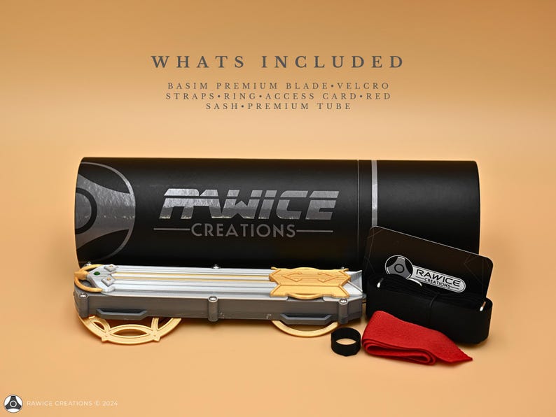 May include: A black tube with the text "Rawice Creations" printed on it. The tube contains a silver and gold blade with a green gem. The image also shows a black strap, a red sash, and a card with the text "Rawice Creations".