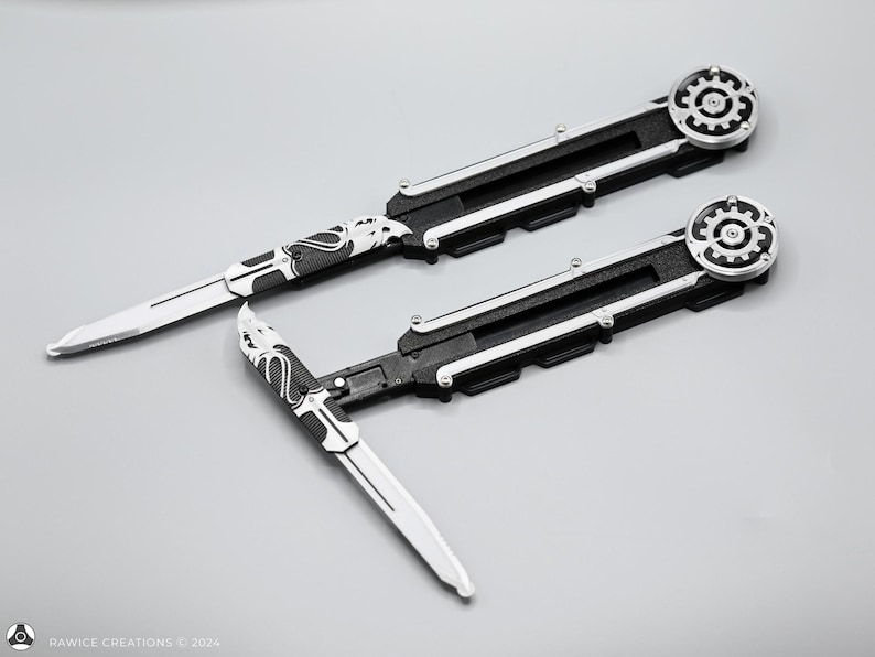 K&ouml;nnte beinhalten: Zwei schwarze und silberne Klappmesser mit einem Zahnrad-Design am Griff. Die Messer haben eine silberne Klinge mit einem schwarz-wei&szlig;en Muster.