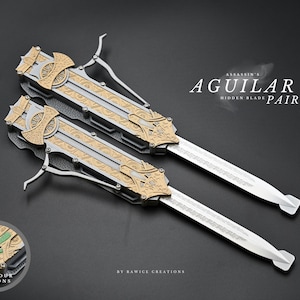 Peut inclure: Une paire de lames cachées Aguilar, avec des lames argentées et des boîtiers décoratifs dorés et argentés. Les lames sont présentées sur un fond sombre, avec le texte "ASSASSIN'S AGUILAR HIDDEN BLADE PAIR".