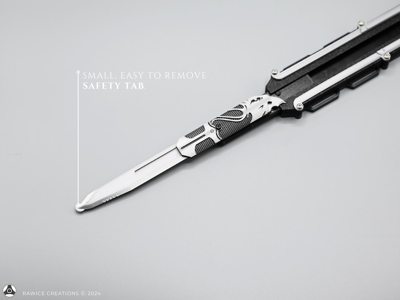 K&ouml;nnte beinhalten: Ein silbernes Klappmesser mit schwarzem Griff und einem Sicherheitsb&uuml;gel mit der Aufschrift "SMALL, EASY TO REMOVE SAFETY TAB".