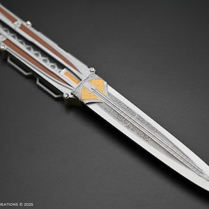 K&ouml;nnte beinhalten: Ein silbernes und goldenes Klappmesser mit einer detaillierten Klinge und komplizierten Mustern. Das Messer ist geschlossen und hat einen braunen Holzgriff.