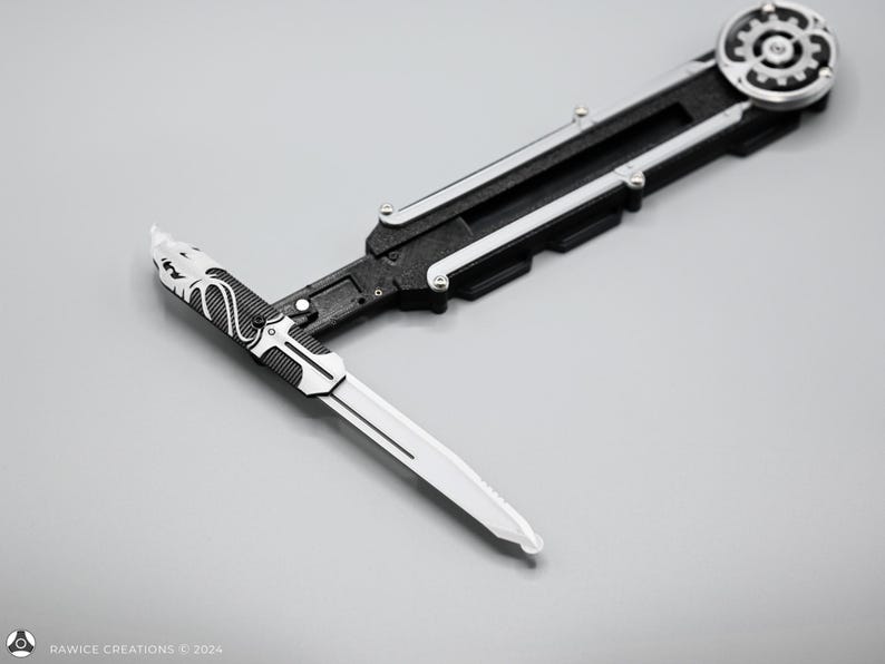 K&ouml;nnte beinhalten: Ein schwarzes und silbernes Klappmesser mit einem detaillierten Design auf der Klinge. Das Messer hat einen zahnradf&ouml;rmigen Mechanismus am Griff.